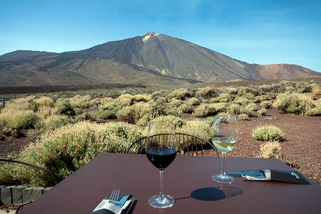 Dos copas de vino sobre una mesa en el Parador Nacional de las Cañadas del Teide, con el majestuoso volcán Teide de fondo.