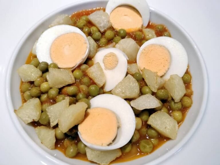 Plato de arvejas con tomate y huevos duros, acompañado de papas fritas.