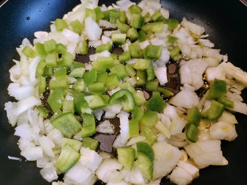 Sofrito de cebolla, ajo y pimiento verde en una sartén.