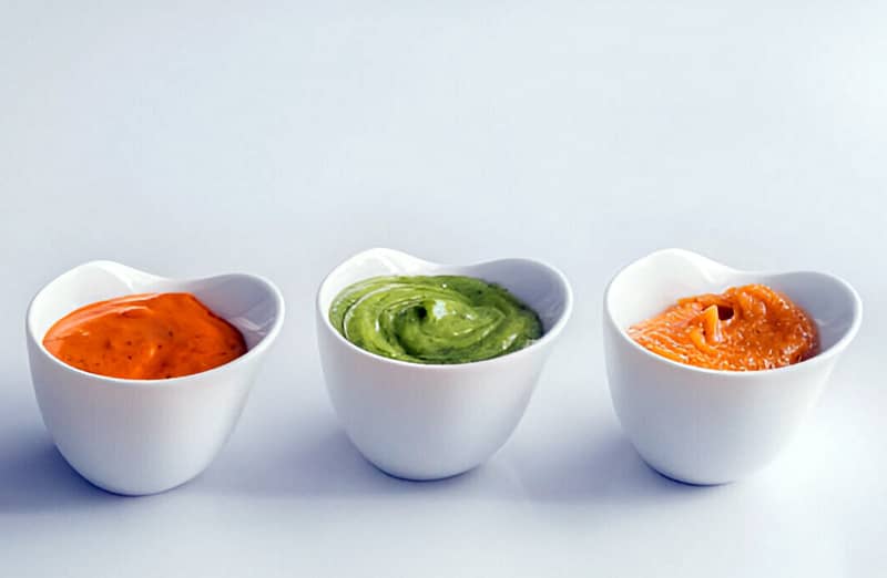 Tres cuencos con mojo picón, mojo verde y mojo rojo con almendras, representando diferentes tipos de mojos canarios.