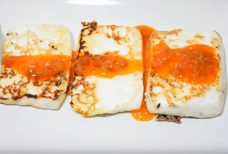 Queso asado con mojo verde y rojo servido en un plato.