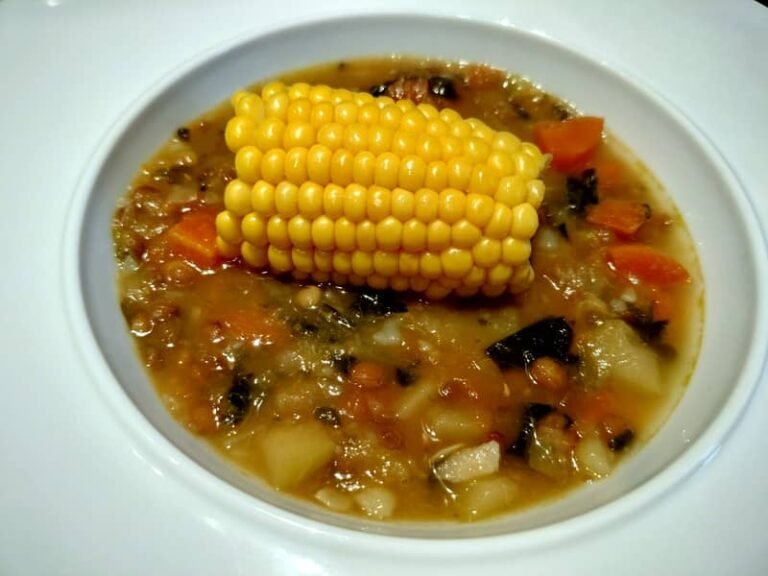 Plato de potaje canario de espinacas y lentejas con un trozo de piña de millo en el centro.