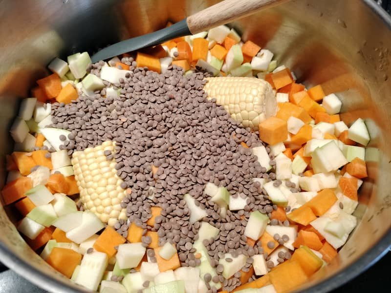 Olla con verduras troceadas, piñas de millo y lentejas listas para cocinar el potaje canario de espinacas y lentejas.